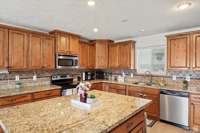 kitchen with stainless steel appliances, a sink, a center island, brown cabinetry, and a textured ceiling