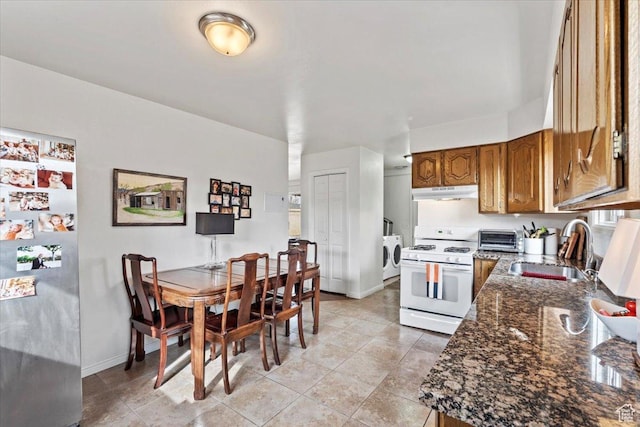 kitchen featuring gas range gas stove, freestanding refrigerator, a sink, under cabinet range hood, and washer and dryer