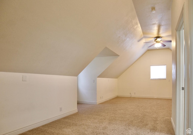 additional living space with ceiling fan, vaulted ceiling, light carpet, baseboards, and a textured ceiling
