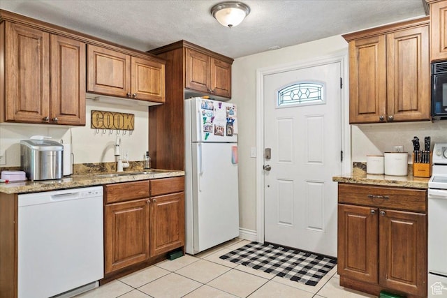 kitchen with white appliances, a sink, light stone countertops, brown cabinetry, and a textured ceiling