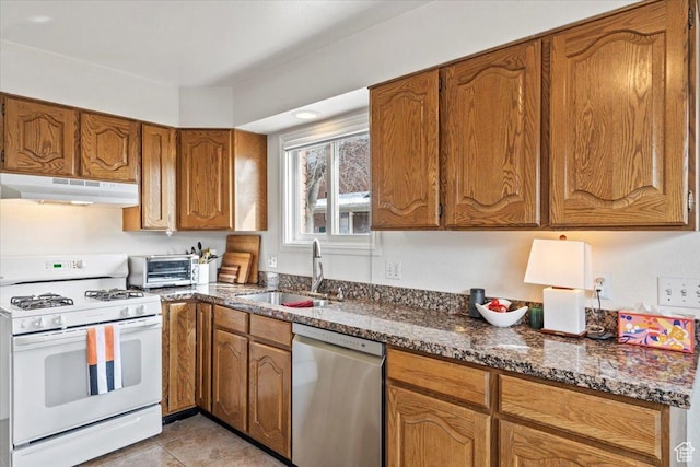 kitchen featuring white gas range, stainless steel dishwasher, under cabinet range hood, a sink, and brown cabinets