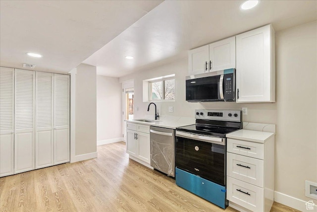 kitchen with appliances with stainless steel finishes, light wood-type flooring, white cabinetry, and a sink