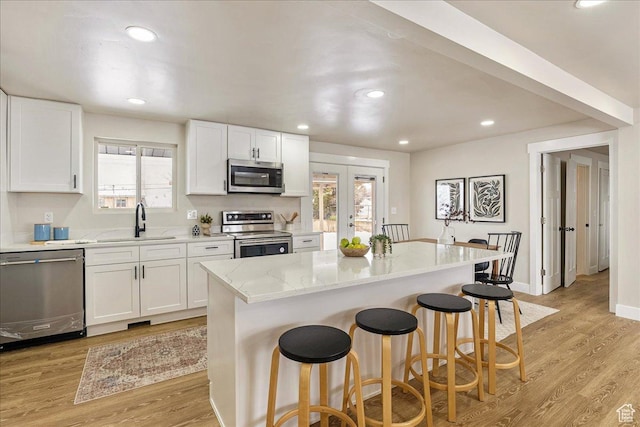 kitchen featuring a breakfast bar, appliances with stainless steel finishes, white cabinetry, a kitchen island, and light stone countertops