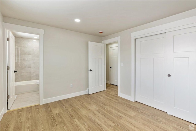 unfurnished bedroom featuring baseboards, a closet, ensuite bath, and light wood-style floors