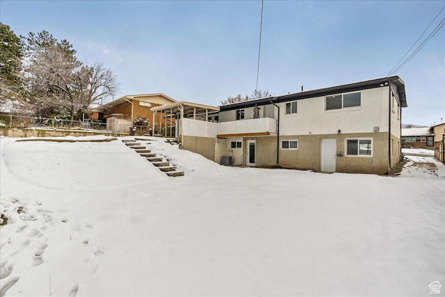 snow covered back of property with cooling unit, brick siding, and fence