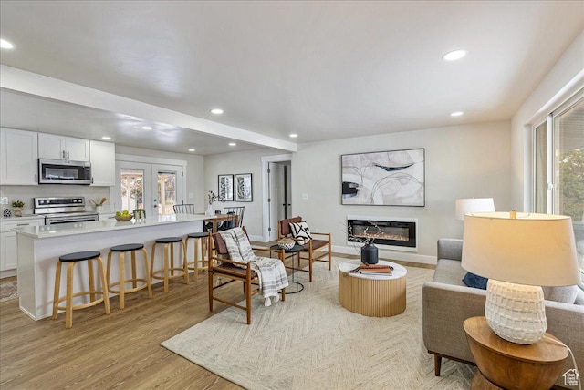 living room featuring a glass covered fireplace, french doors, light wood finished floors, and recessed lighting