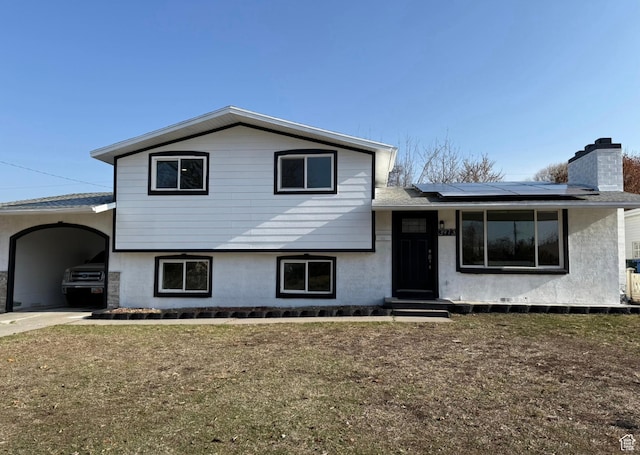 split level home featuring solar panels, a chimney, a front lawn, a carport, and stucco siding