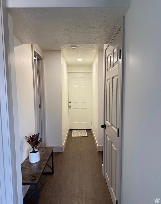 hallway with dark wood-style floors, a textured ceiling, and baseboards