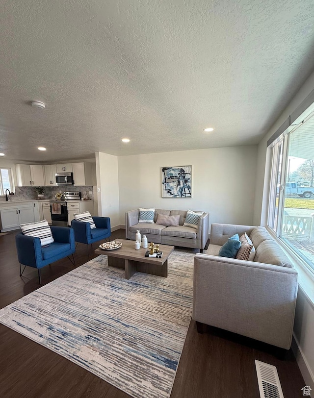 living room with dark wood-style floors, visible vents, and a wealth of natural light