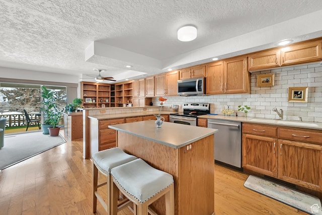 kitchen featuring stainless steel appliances, a sink, a textured ceiling, a center island, and a ceiling fan