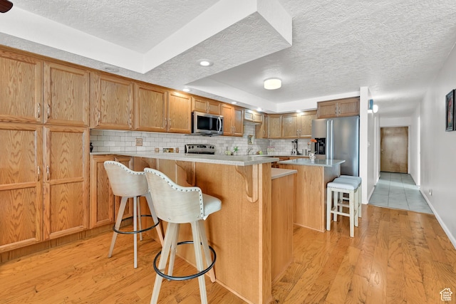 kitchen with appliances with stainless steel finishes, a textured ceiling, a kitchen bar, light wood-type flooring, and tasteful backsplash