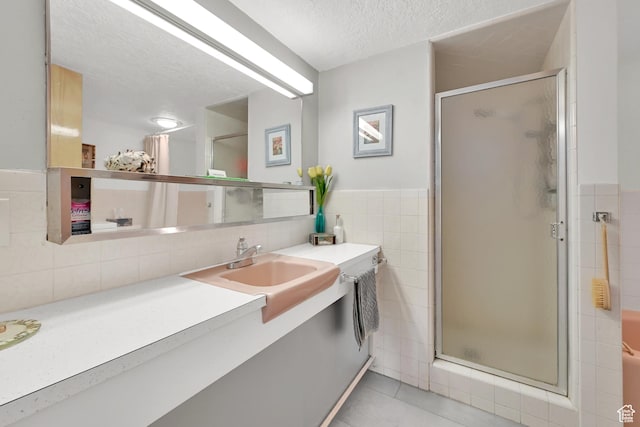 bathroom with tile walls, a shower stall, a textured ceiling, tile patterned flooring, and vanity