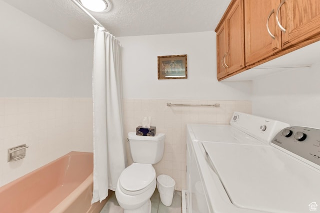 clothes washing area with washing machine and clothes dryer, wainscoting, a textured ceiling, tile walls, and light tile patterned floors