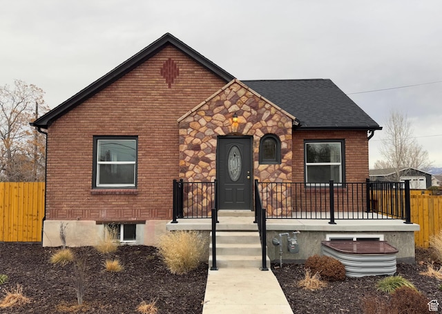 view of front of home featuring a shingled roof, stone siding, brick siding, and fence