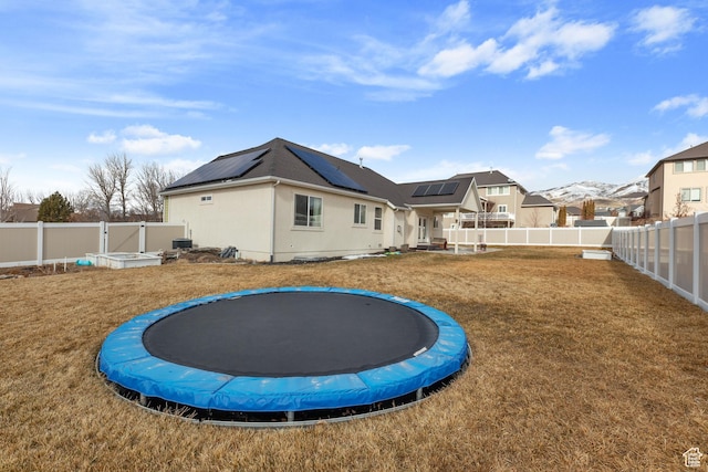 rear view of property with solar panels, a yard, a trampoline, and a fenced backyard