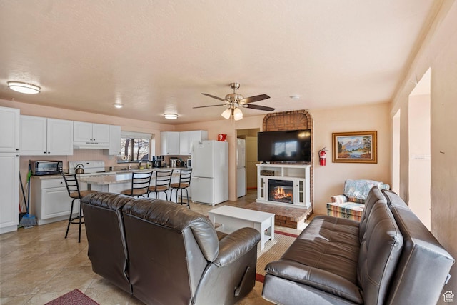 living room with a ceiling fan, a fireplace, and a textured ceiling