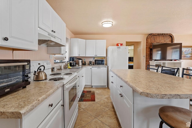 kitchen featuring white appliances, white cabinets, a breakfast bar, light countertops, and under cabinet range hood