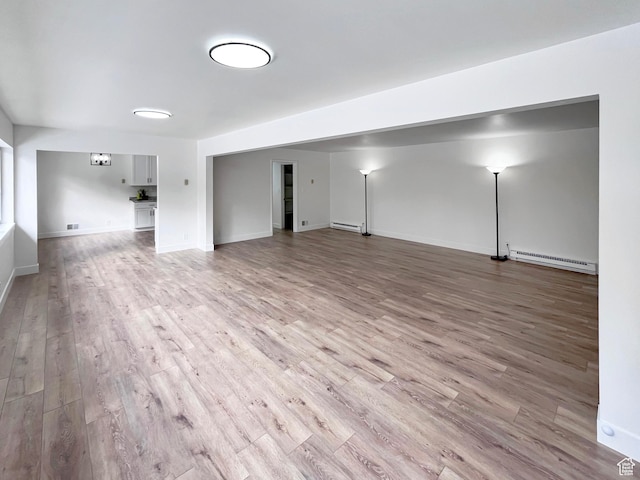 unfurnished living room with light wood-type flooring, a baseboard radiator, and baseboards
