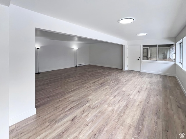unfurnished room featuring baseboards, baseboard heating, and wood finished floors
