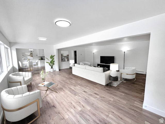 living area with a baseboard heating unit, wood finished floors, and baseboards