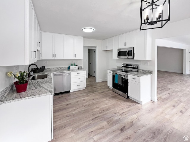 kitchen featuring white cabinets, appliances with stainless steel finishes, hanging light fixtures, light stone countertops, and a sink