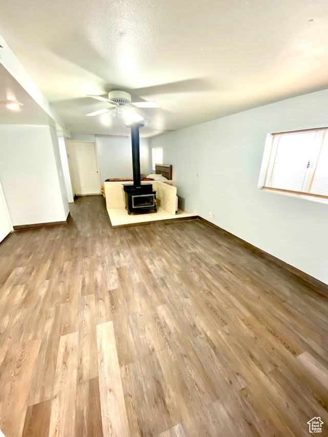5444 W Bailiff Dr S, Kearns, UT 84118 - unfurnished living room featuring a textured ceiling, baseboards, wood finished floors, a ceiling fan, and a wood stove