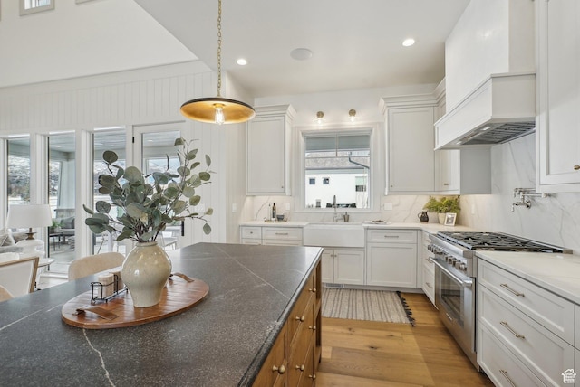 kitchen featuring pendant lighting, light wood-style flooring, white cabinetry, a sink, and high end range