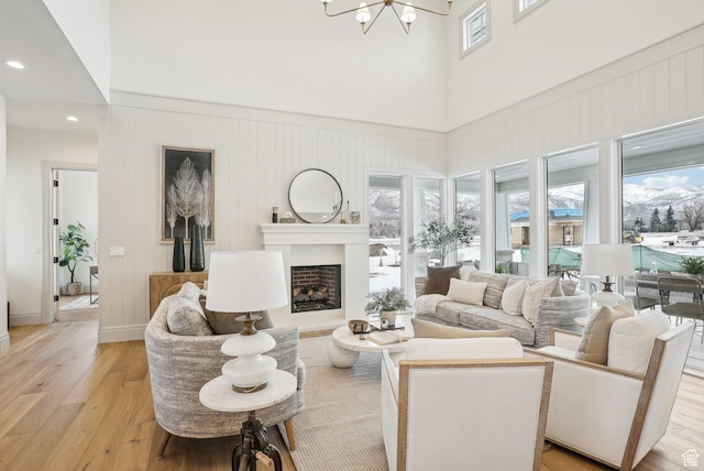 living room featuring light wood-style flooring, a fireplace, a high ceiling, and a chandelier
