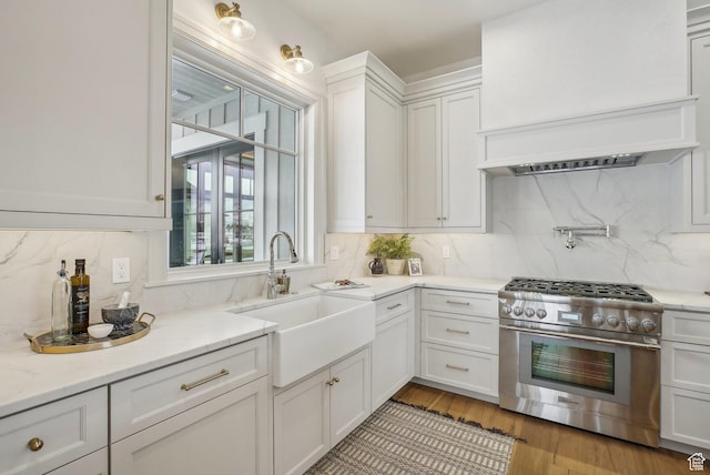 kitchen with white cabinets, light wood-style flooring, high end stainless steel range oven, custom exhaust hood, and a sink