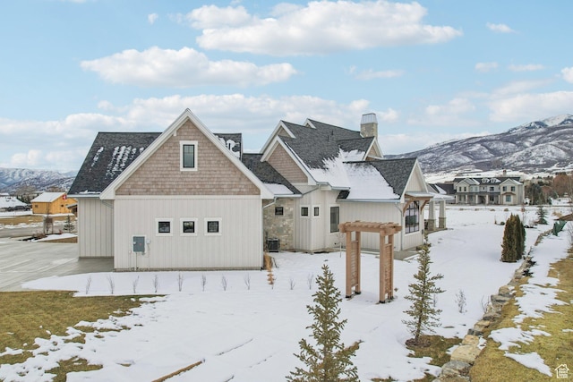 snow covered rear of property featuring a chimney and a mountain view