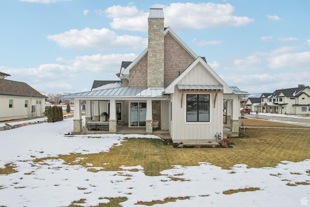 snow covered property featuring a porch, board and batten siding, a residential view, a standing seam roof, and a chimney
