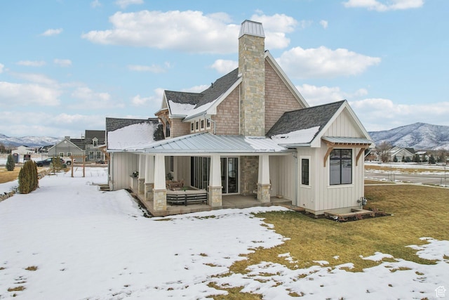 snow covered property with a lawn, board and batten siding, a standing seam roof, a mountain view, and metal roof
