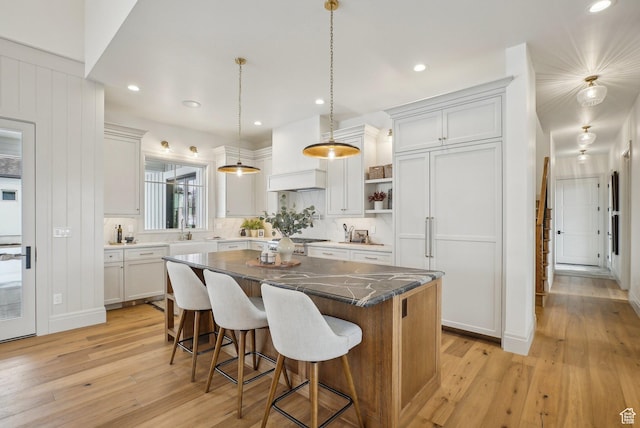 kitchen featuring a center island, decorative light fixtures, white cabinets, light wood-type flooring, and a kitchen breakfast bar
