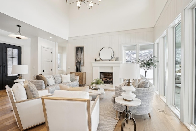 living room featuring a towering ceiling, light wood-style flooring, a fireplace, and visible vents