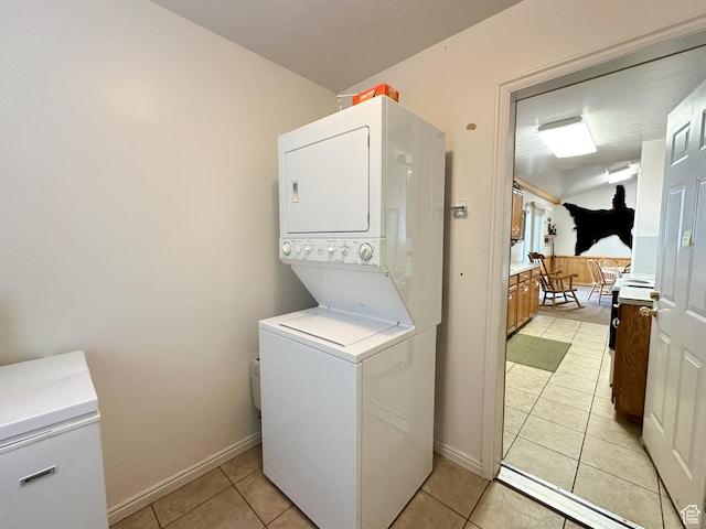 laundry room with light tile patterned floors, baseboards, laundry area, and stacked washer and clothes dryer