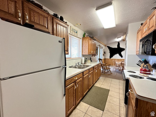 kitchen with electric range oven, freestanding refrigerator, light countertops, black microwave, and a sink