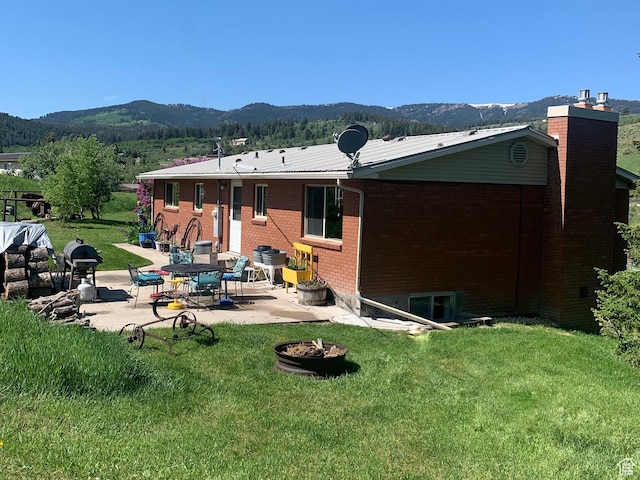 322 Bailey Rd, Soda Springs, ID 83276 - rear view of property featuring a mountain view, a patio, brick siding, an outdoor fire pit, and a lawn