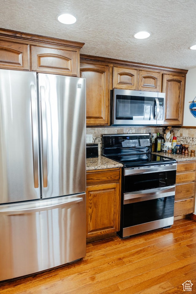 322 Bailey Rd, Soda Springs, ID 83276 - kitchen featuring stainless steel appliances, decorative backsplash, brown cabinets, light wood-type flooring, and a textured ceiling
