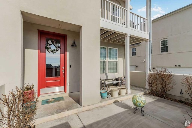 view of exterior entry featuring a balcony and stucco siding