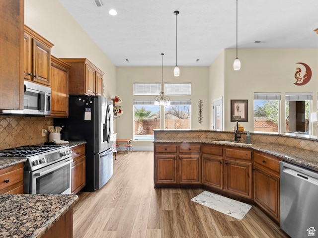 1908 S Yuma Dr, Washington, UT 84780 - kitchen with appliances with stainless steel finishes, brown cabinets, light wood-type flooring, decorative backsplash, and pendant lighting