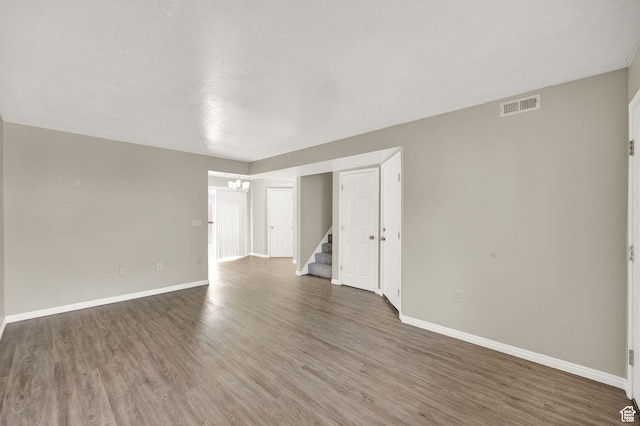 spare room with dark wood-style floors, visible vents, baseboards, and stairs
