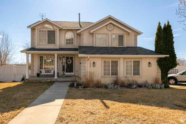 traditional-style house with a front yard, covered porch, fence, and stucco siding