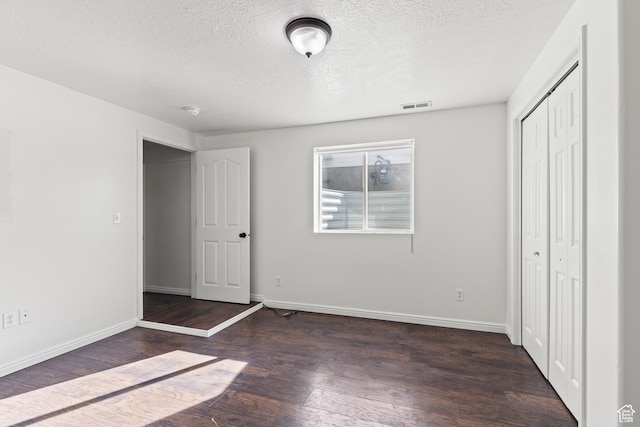 257 Rosewood Cir, Logan, UT 84321 - unfurnished bedroom featuring a textured ceiling, visible vents, baseboards, a closet, and dark wood finished floors