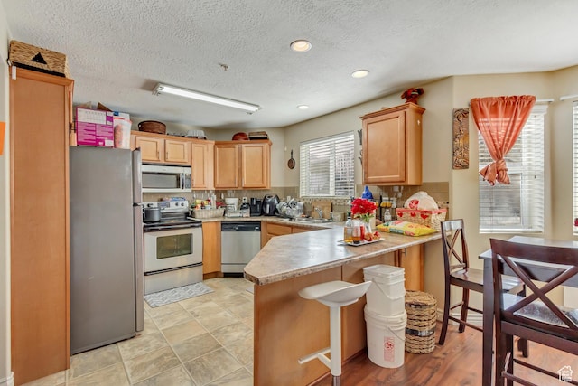 3842 S Clare Dr Unit D-1, West Valley City, UT 84119 - kitchen with a peninsula, light countertops, appliances with stainless steel finishes, backsplash, and a kitchen bar