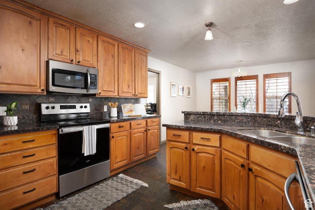 kitchen featuring tasteful backsplash, dark countertops, brown cabinets, stainless steel appliances, and a sink