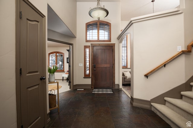 entrance foyer featuring stone finish floor, a towering ceiling, baseboards, and stairs