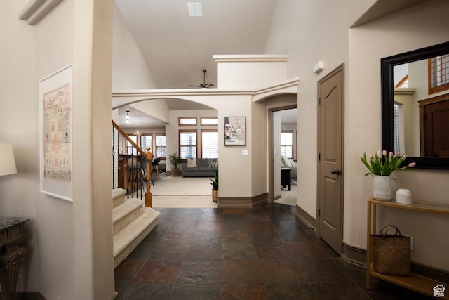 entrance foyer with baseboards, arched walkways, stairway, stone tile flooring, and high vaulted ceiling