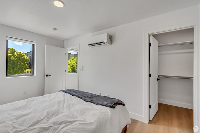 bedroom with baseboards, light wood-style floors, and a wall unit AC