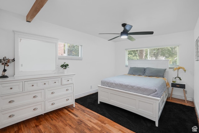 bedroom featuring ceiling fan, baseboards, wood finished floors, and beamed ceiling