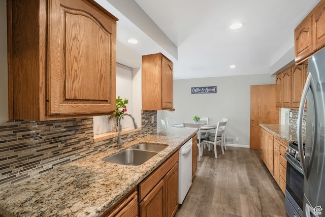 kitchen featuring tasteful backsplash, appliances with stainless steel finishes, brown cabinetry, a sink, and light stone countertops